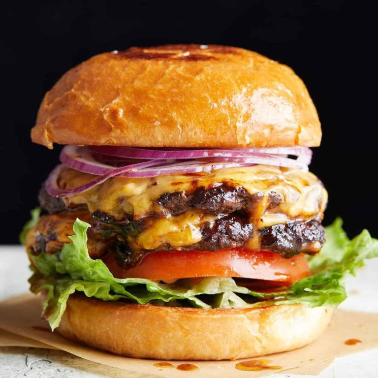 A rich double cheeseburger with melted cheese, red onion, tomato, and lettuce inside a toasted bun
