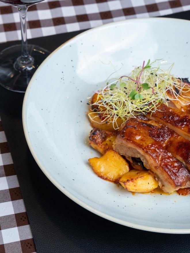 Juicy slices of roasted meat with potatoes and sprouts, served at a table next to a glass of red wine