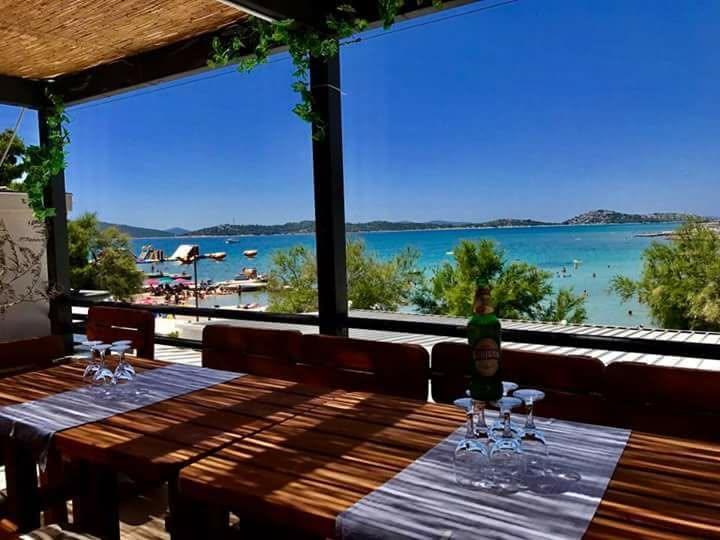 Beautiful open view from the covered terrace of Vidikovac restaurant over wooden tables looking out to the crystal turquoise sea and beach in Vodice