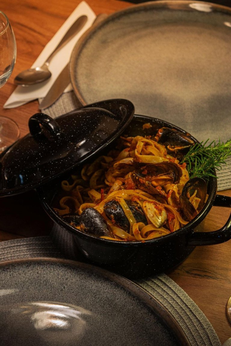 Homemade seafood pasta with mussels and clams in tomato sauce served in a black pot at Restoran i Catering Roko in Bjelovar