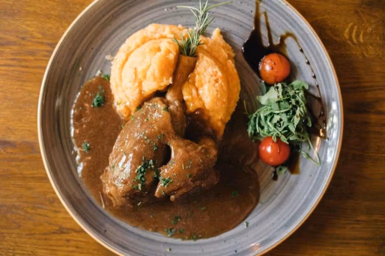 Tender braised meat shank served with smooth potato-carrot puree and rich gravy at Bistro & Pizzeria Piccolo in Zagreb