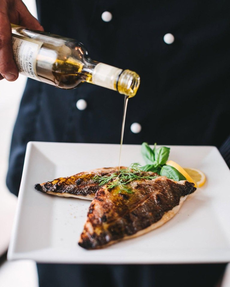 Chef drizzling olive oil over freshly grilled fish fillets at Dalmatino Grill & Pizza Zagreb