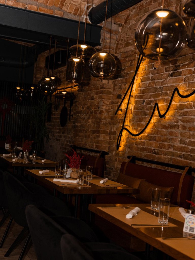 Elegant restaurant atmosphere at Restoran Lu in Vinkovci featuring illuminated wall signage on brick and set tables